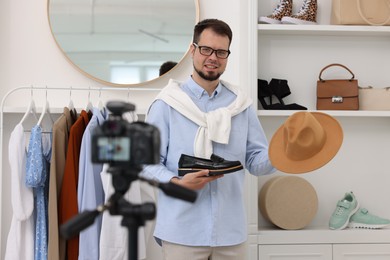 Photo of Smiling fashion blogger showing shoe and hat while recording video at home