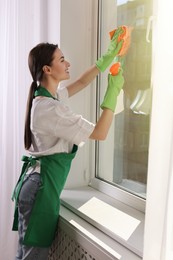 Young woman cleaning window glass with rag and detergent at home