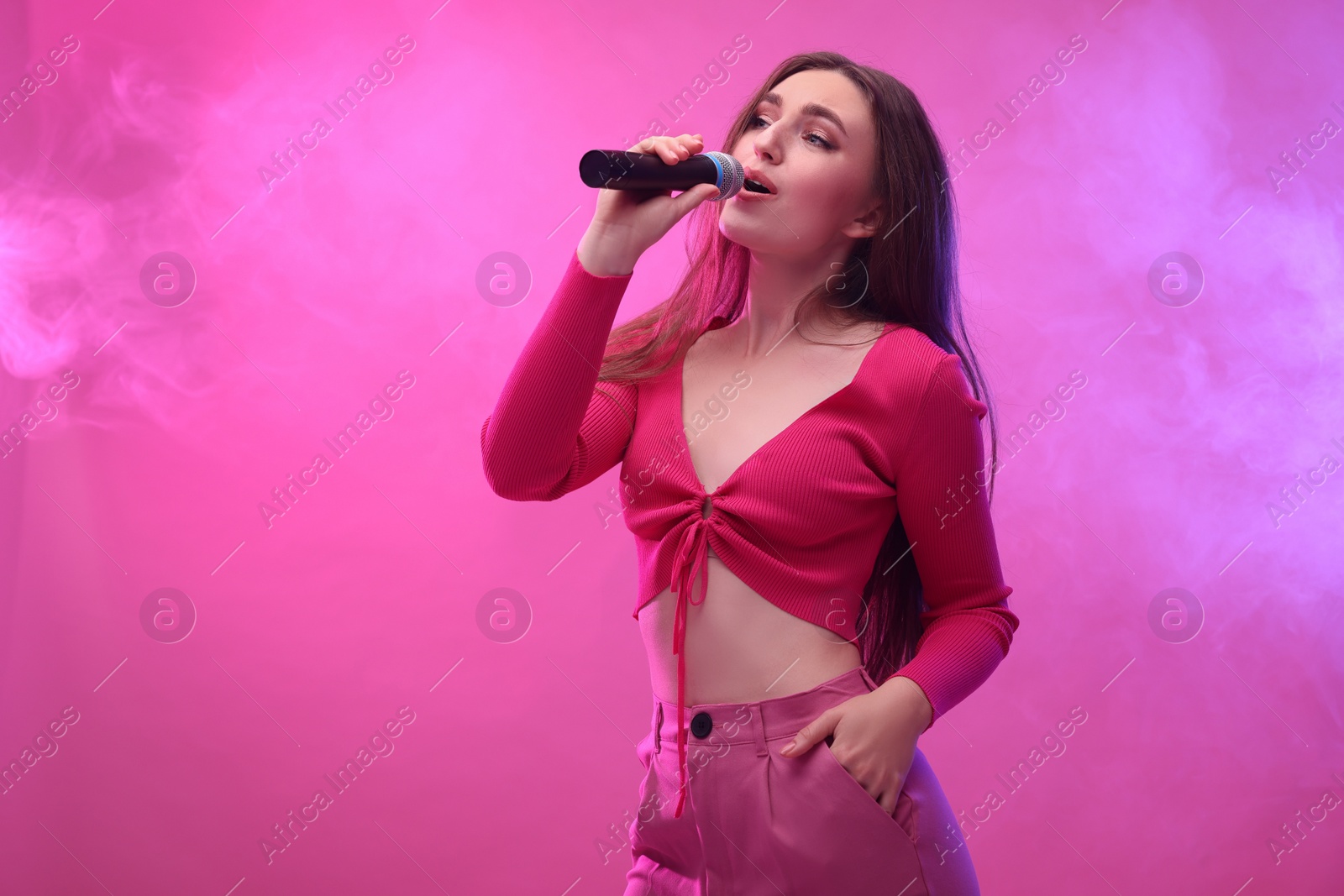 Photo of Emotional woman with microphone singing on pink background. Space for text