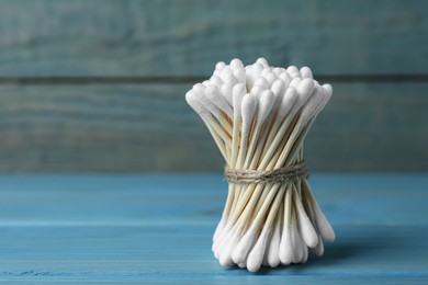 Many cotton buds on light blue wooden table, space for text