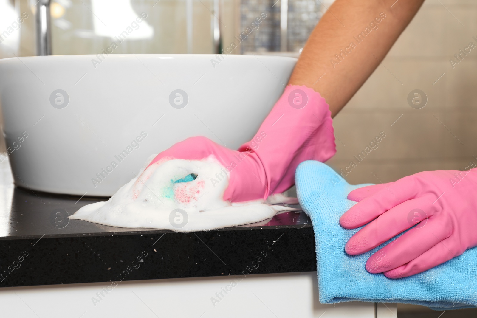 Photo of Woman in protective gloves cleaning bathroom countertop with sponge, closeup