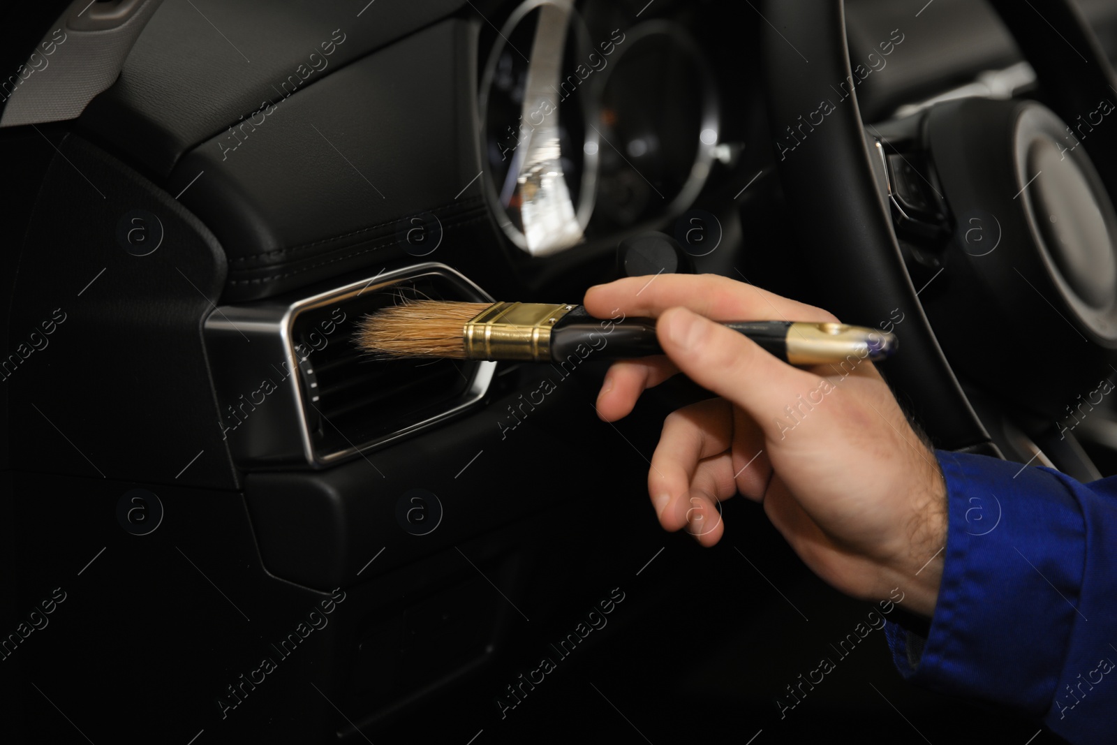 Photo of Worker cleaning automobile air conditioner vent grill with brush, closeup. Car wash service