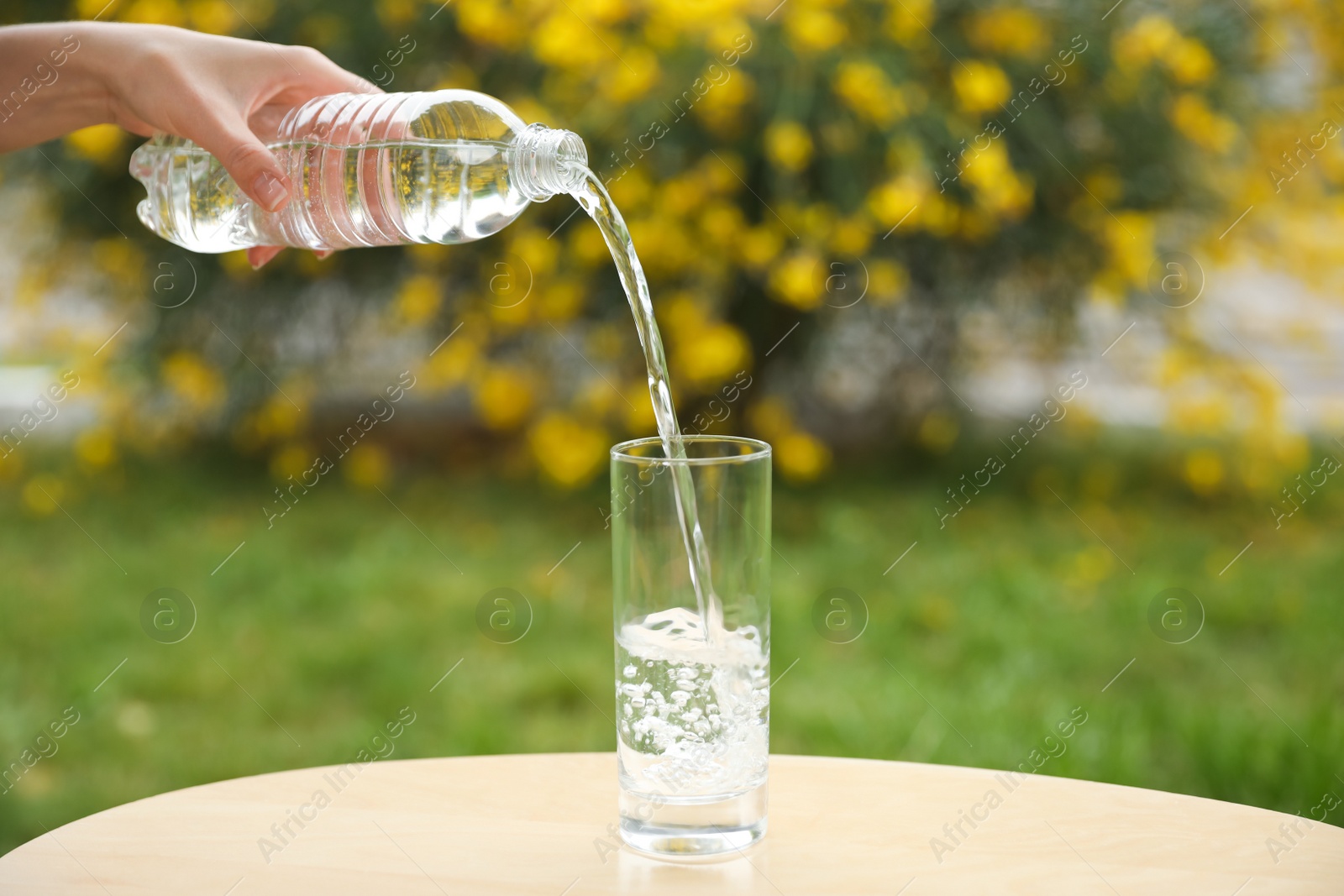 Photo of Woman pouring water from bottle into glass on table outdoors, closeup