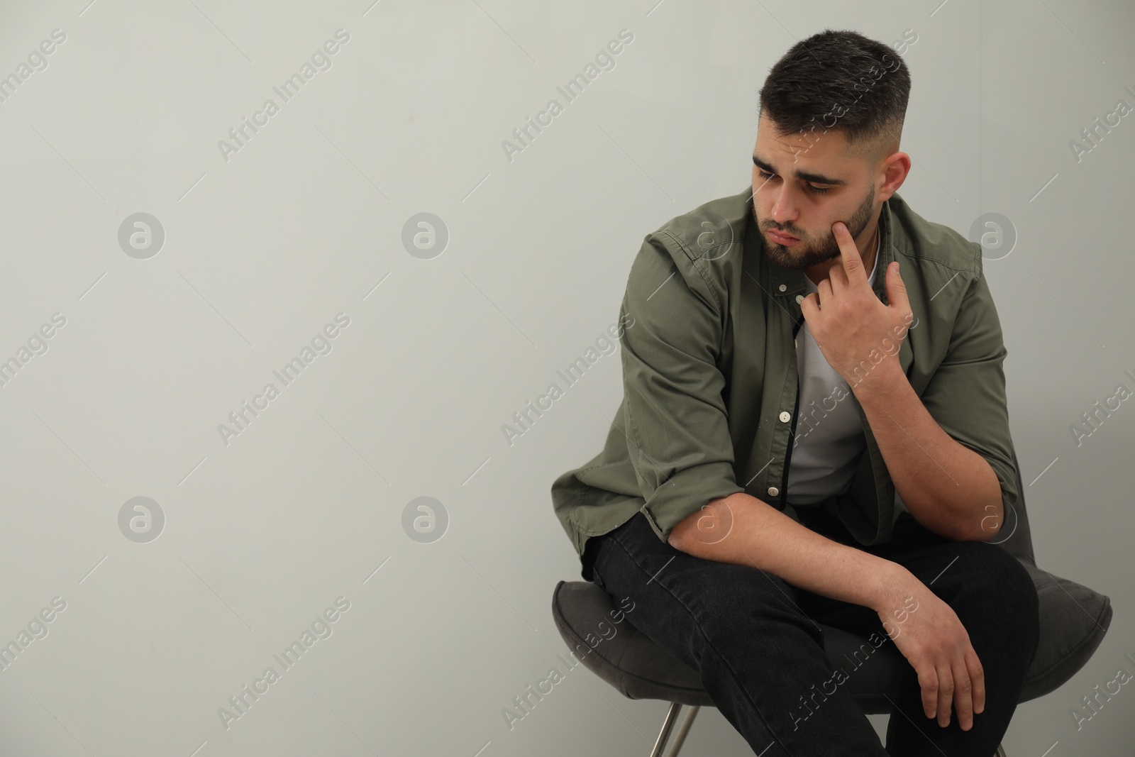 Photo of Sad man sitting near light grey wall. Space for text