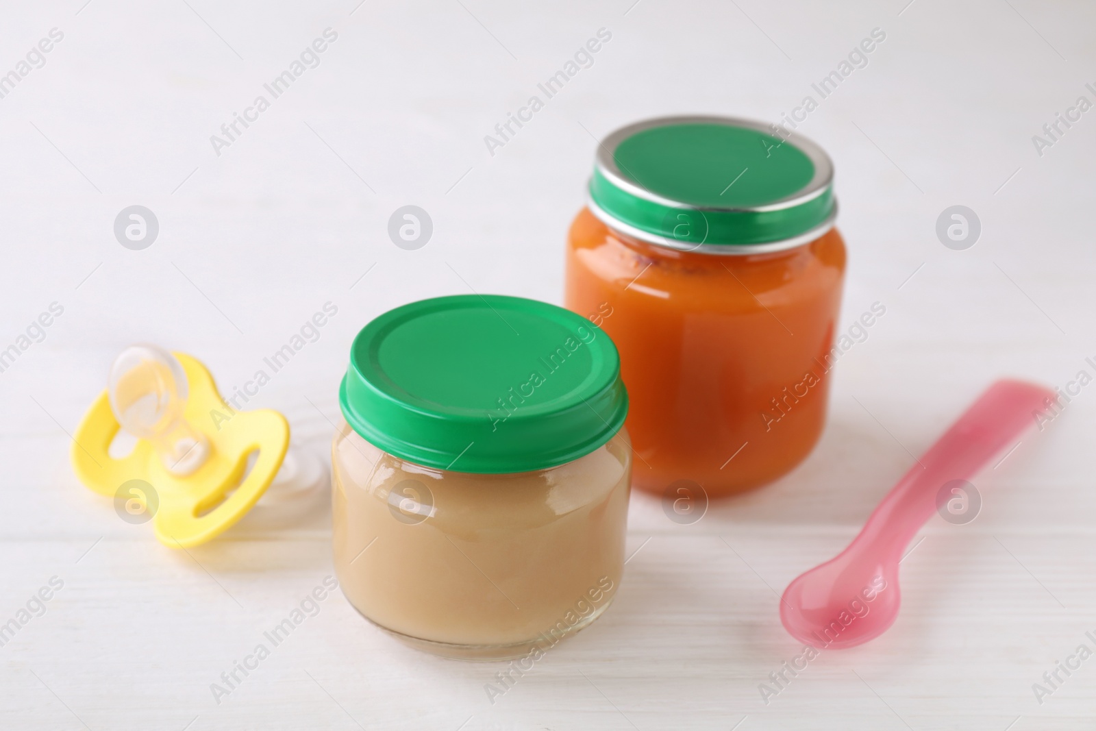 Photo of Jars with healthy baby food, spoon and pacifier on white wooden table