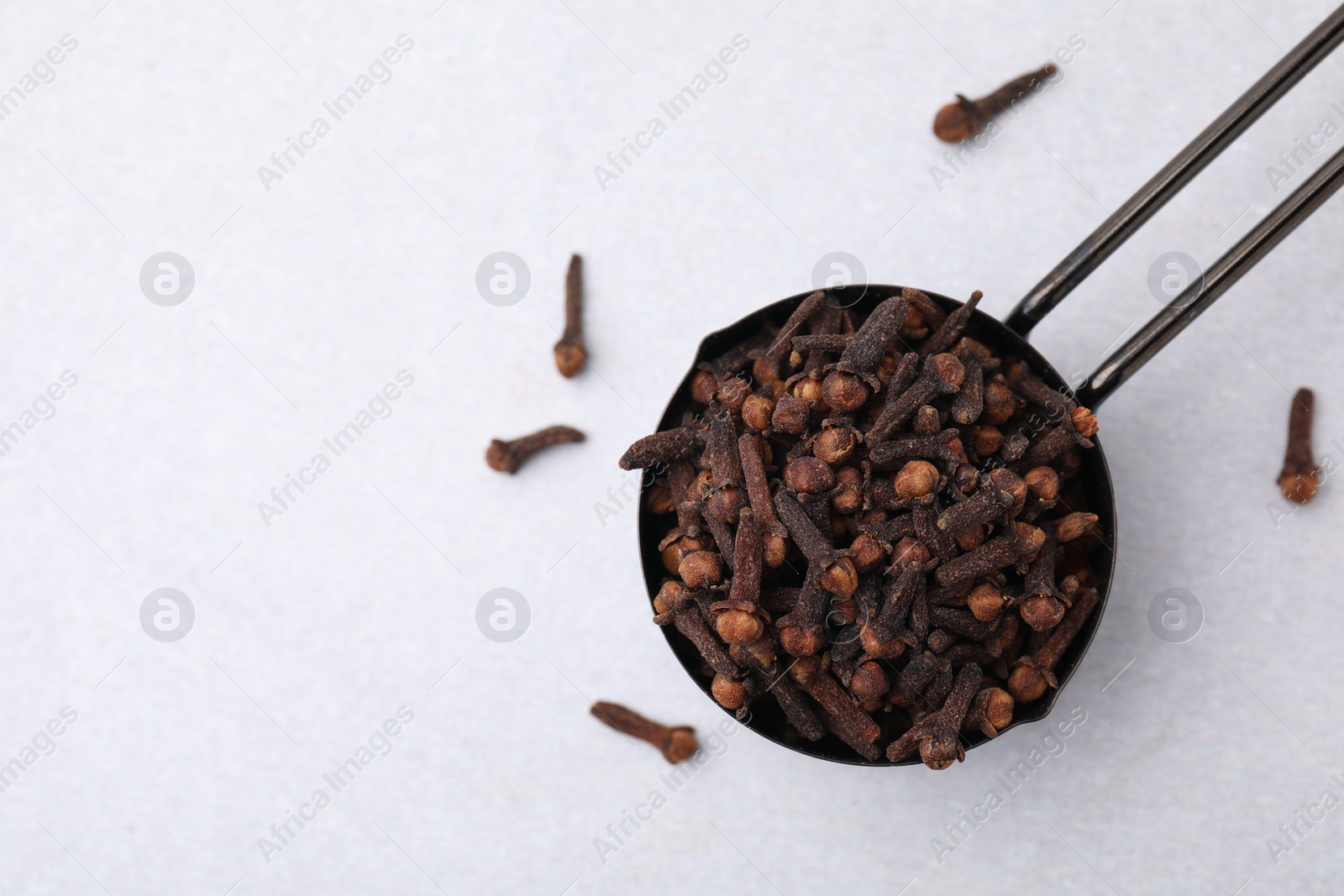 Photo of Aromatic cloves in scoop on light table, top view. Space for text