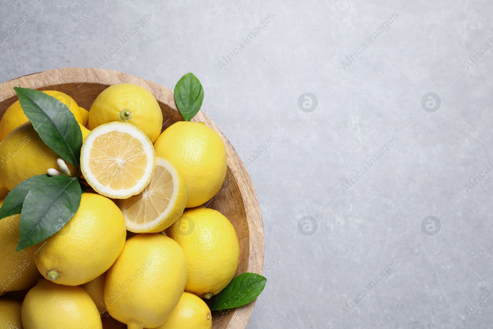 Photo of Many fresh ripe lemons with green leaves on light grey table, top view. Space for text