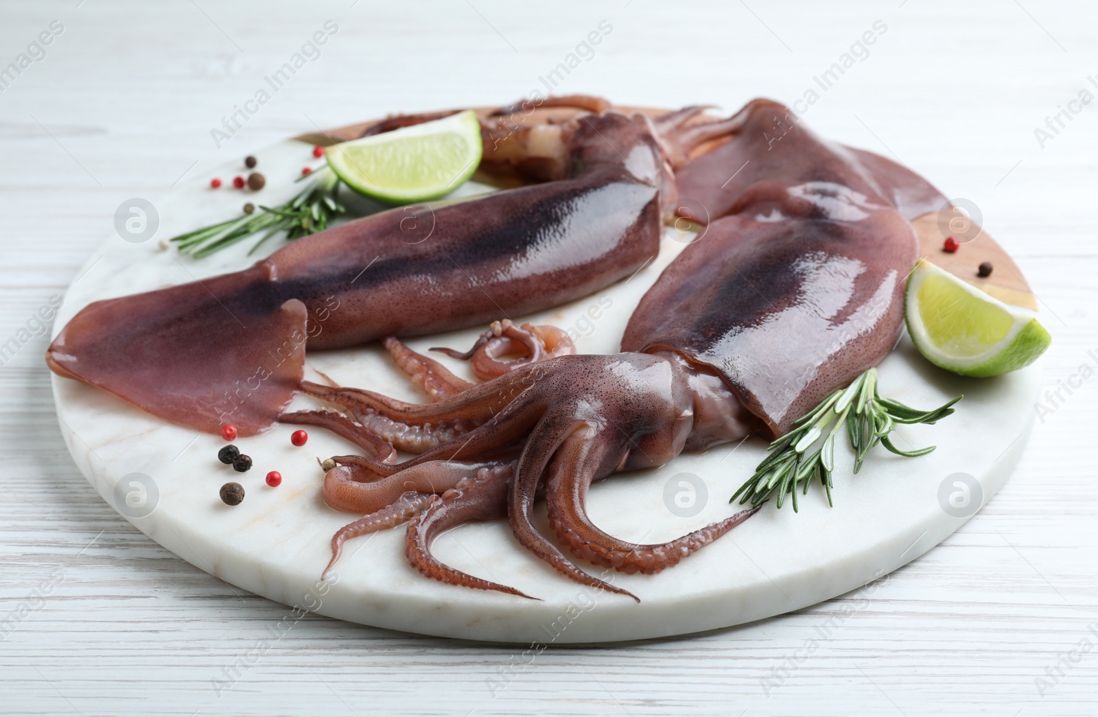 Photo of Fresh raw squids with lime and rosemary on white wooden table