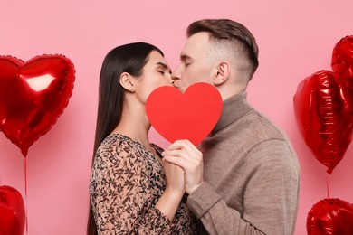 Lovely couple kissing behind red paper heart on pink background. Valentine's day celebration