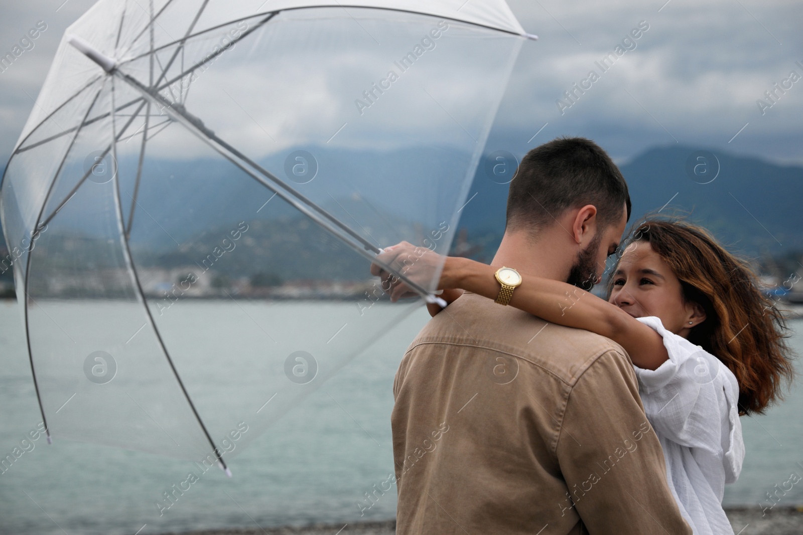 Photo of Young couple with umbrella enjoying time together under rain on beach