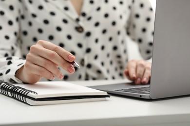 Photo of E-learning. Woman taking notes during online lesson at table indoors, closeup