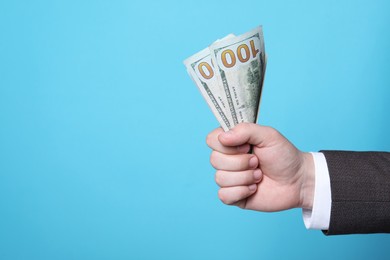 Man holding money on light blue background, closeup. Space for text. Currency exchange