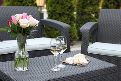 Vase with roses, glasses of wine and food on rattan table on outdoor terrace