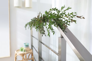 Photo of Beautiful garland made of eucalyptus branches on handrail indoors