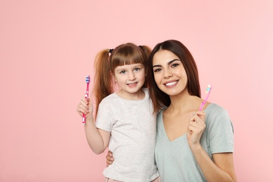 Photo of Little girl and her mother with toothbrushes on color background. Teeth care