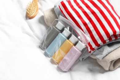 Photo of Cosmetic travel kit. Plastic bag with small containers of personal care products and stack of clothes on bed