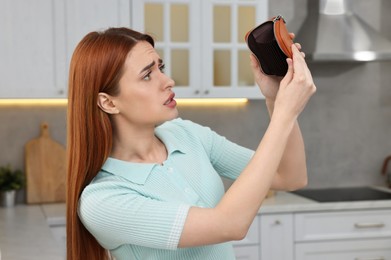 Upset woman with empty wallet at home