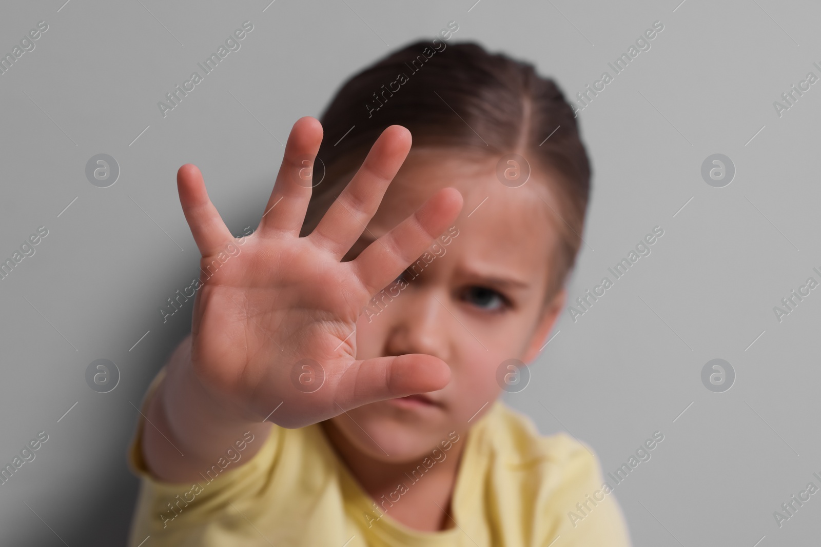 Photo of Child abuse. Girl making stop gesture near grey wall, selective focus