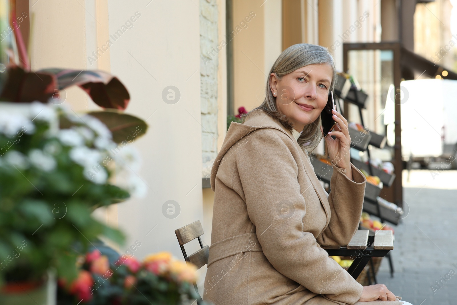 Photo of Beautiful senior woman sitting and talking on smartphone outdoors, space for text