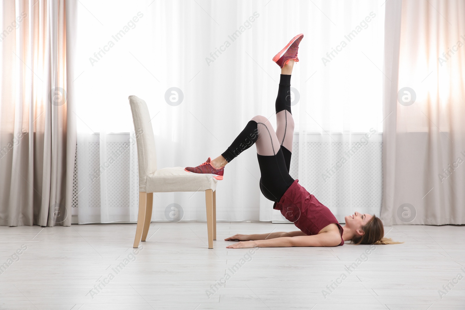 Photo of Young woman exercising with chair indoors. Home fitness