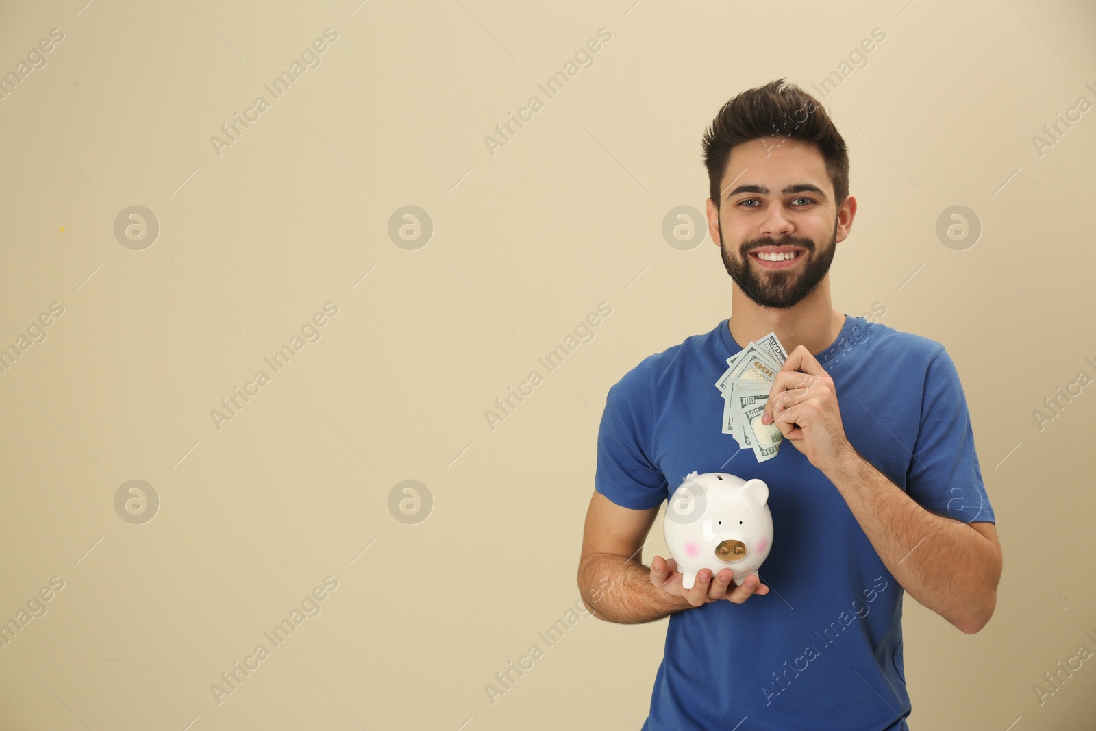 Photo of Portrait of happy young man with money and piggy bank on color background. Space for text