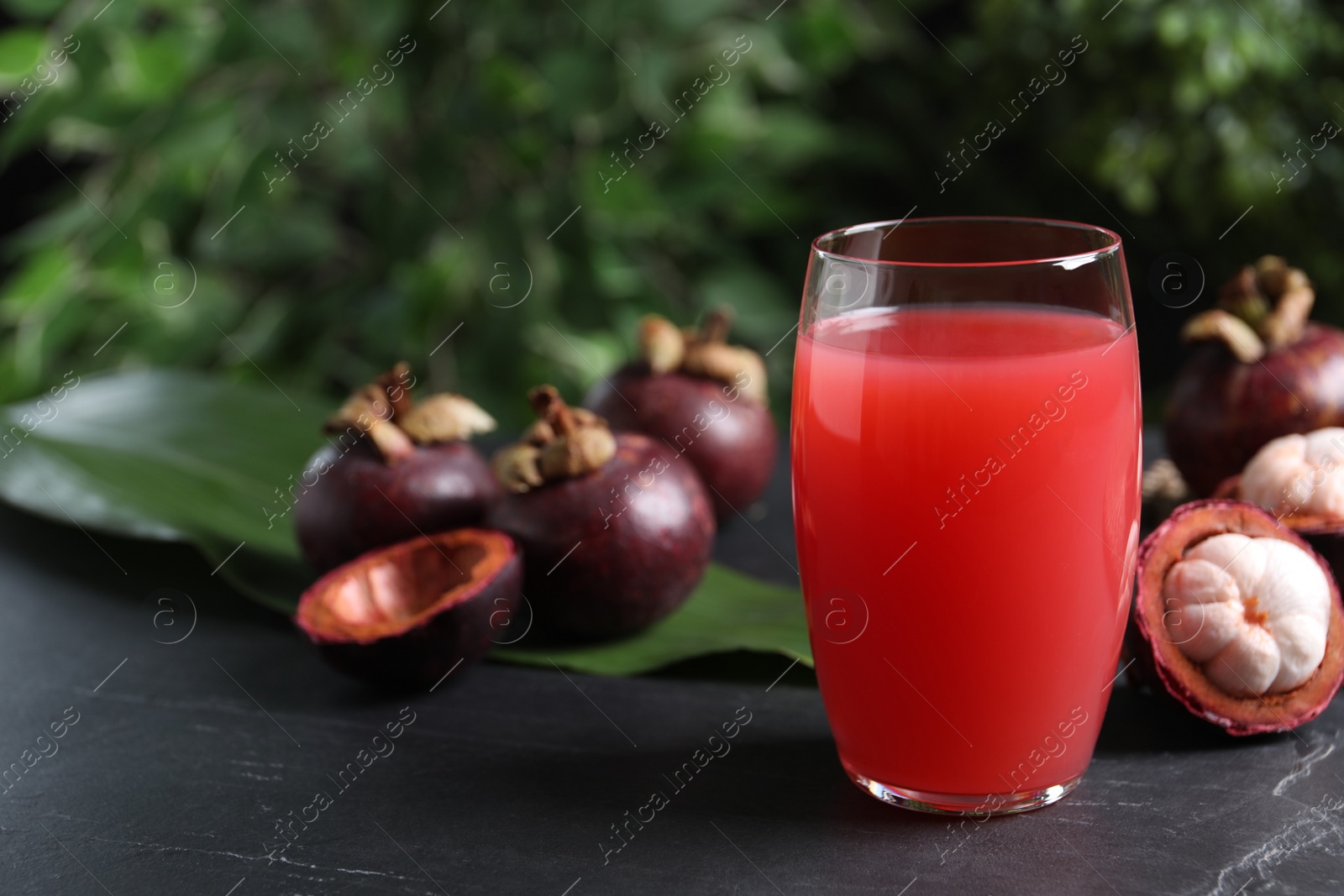 Photo of Delicious mangosteen juice in glass on dark table, space for text