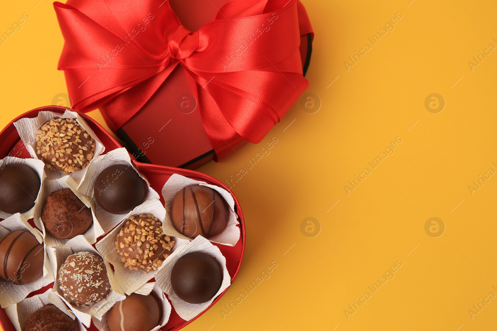 Photo of Heart shaped box with delicious chocolate candies on yellow background, flat lay. Space for text