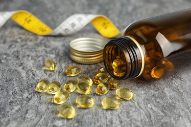 Bottle with cod liver oil pills and measuring tape on table, closeup