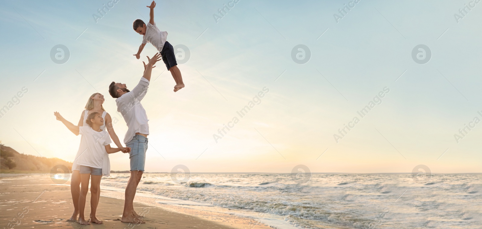 Image of Happy family having fun on sandy beach near sea at sunset, space for text. Banner design