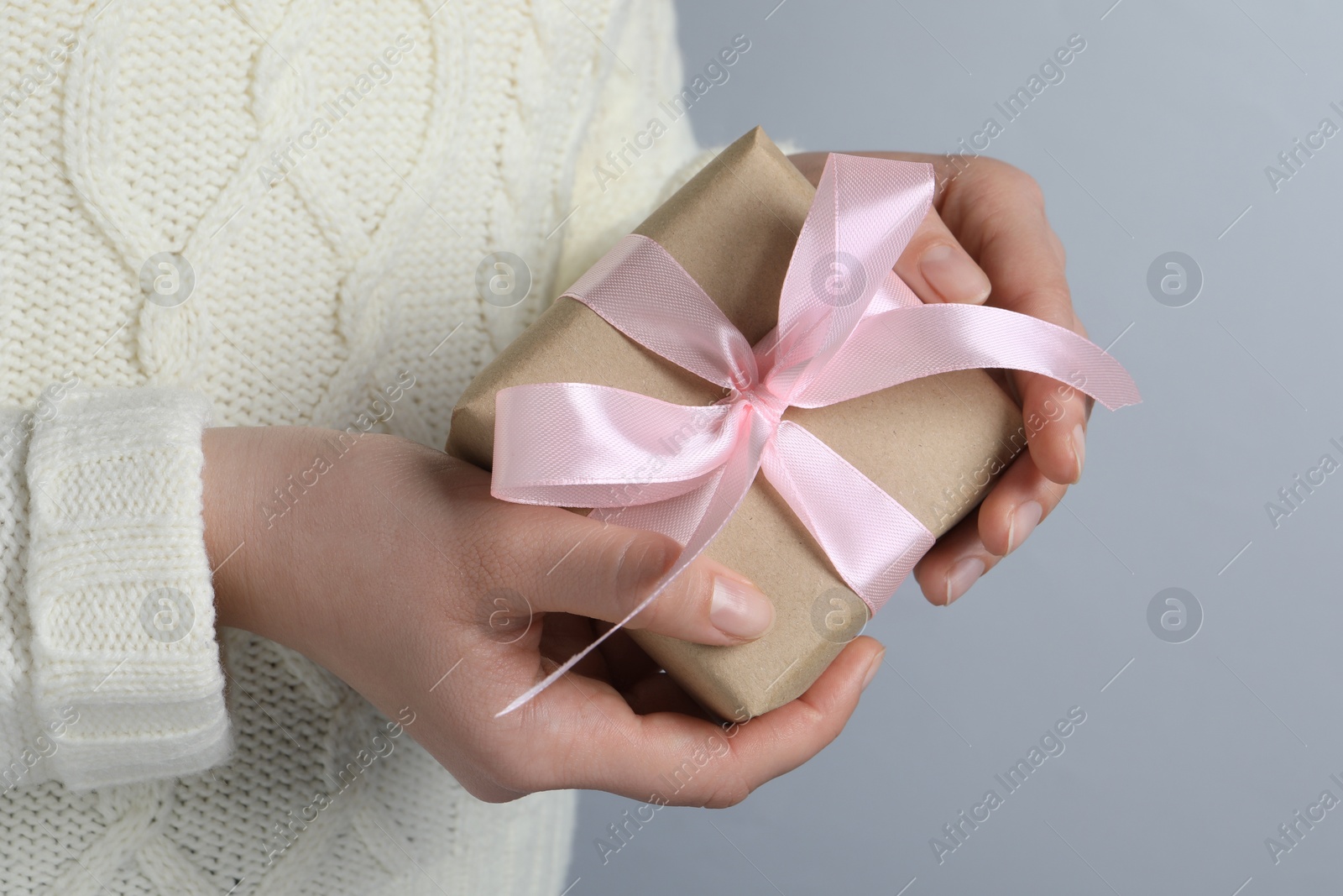 Photo of Woman holding gift box with pink bow on light grey background, closeup