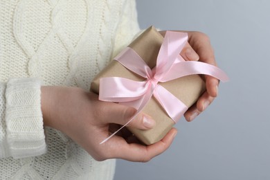 Photo of Woman holding gift box with pink bow on light grey background, closeup