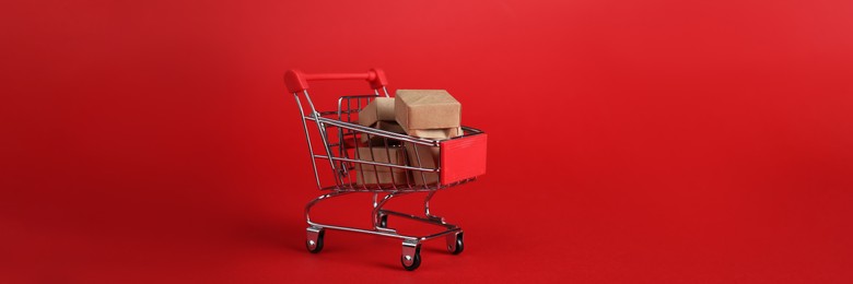 Photo of Small metal shopping cart with cardboard boxes on red background