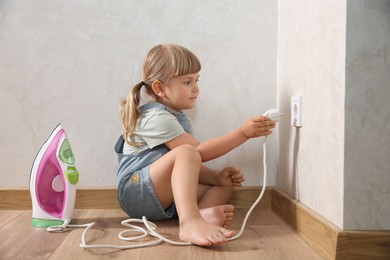 Photo of Little child playing with electrical socket and iron plug at home. Dangerous situation