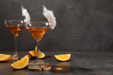 Photo of Tasty cocktails in glasses decorated with cotton candy and orange slices on gray table, space for text