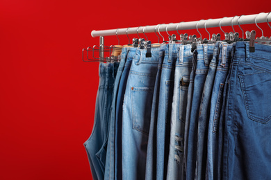 Rack with different jeans on red background