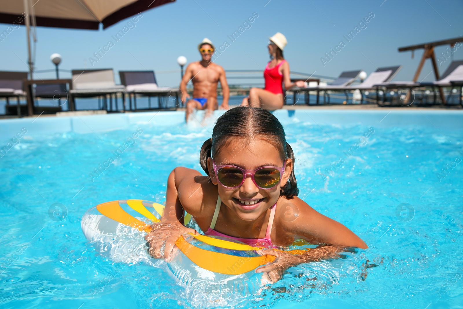 Photo of Happy girl and her parents having fun in swimming pool. Family vacation