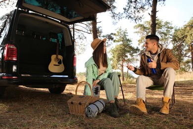 Photo of Couple with thermos and picnic basket resting in camping chairs outdoors