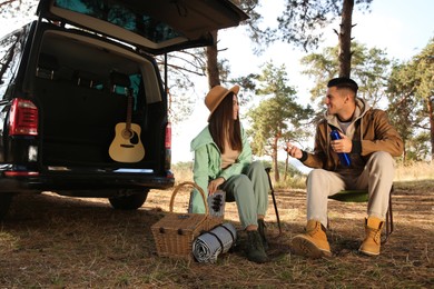 Couple with thermos and picnic basket resting in camping chairs outdoors