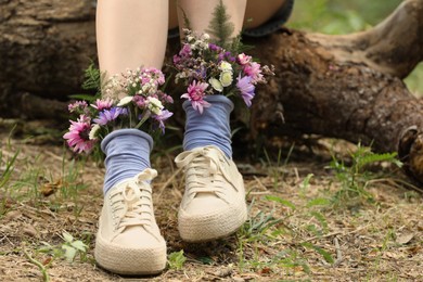 Photo of Woman sitting on log with flowers in socks outdoors, closeup