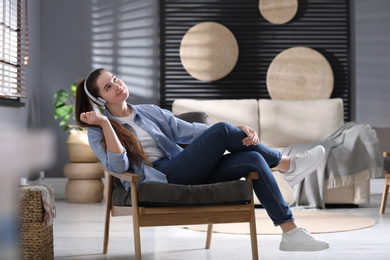 Photo of Young woman with headphones listening to music in armchair at home
