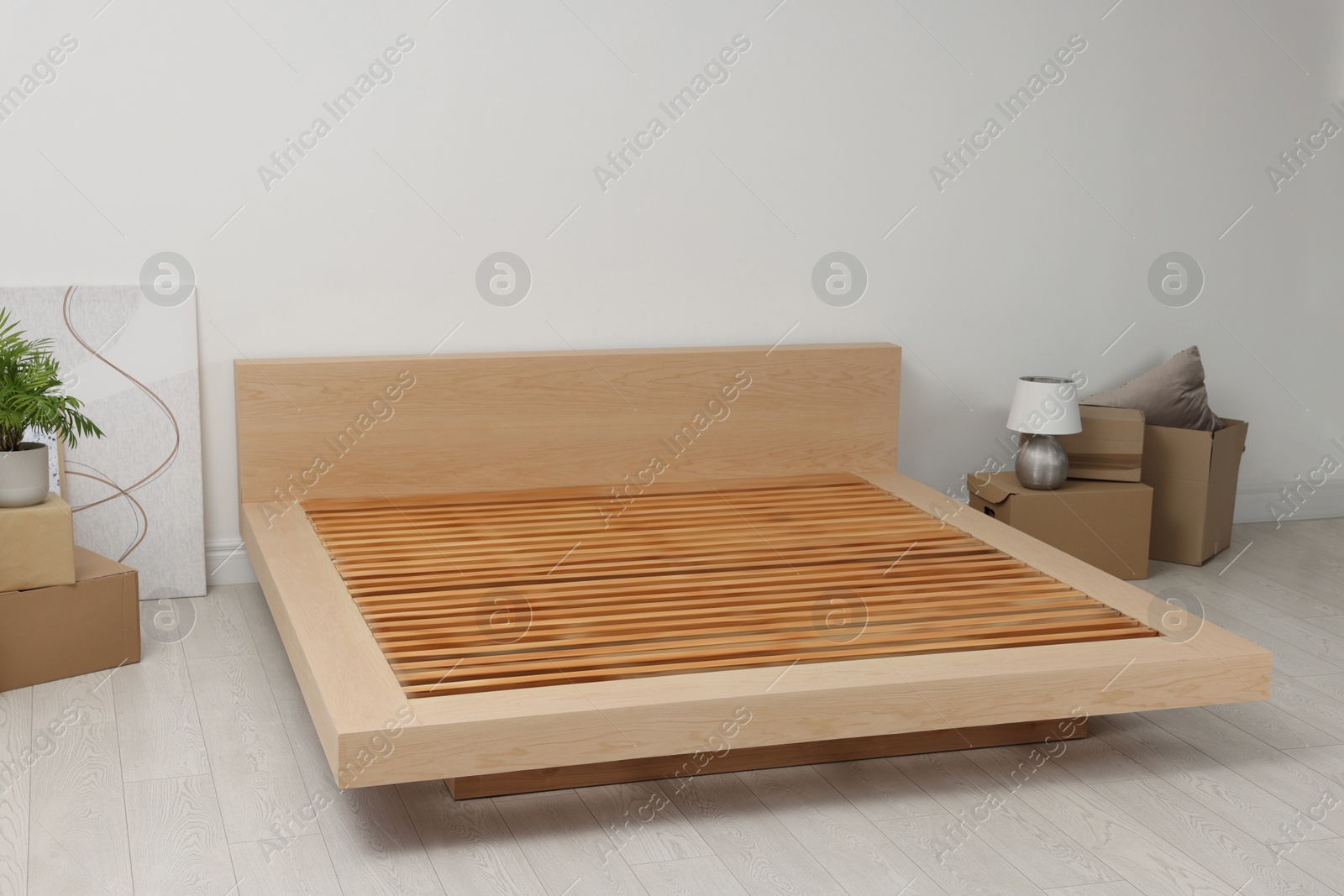 Photo of New wooden bed frame, moving boxes and decor elements indoors