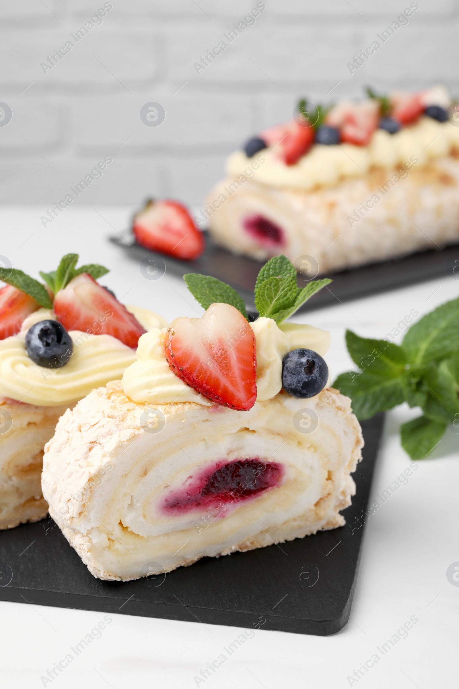 Photo of Pieces of tasty meringue roll with jam, cream, strawberry, blueberry and mint on white table