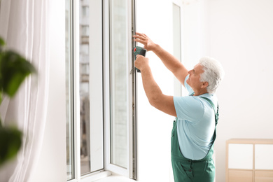 Photo of Mature construction worker repairing plastic window with electric screwdriver indoors