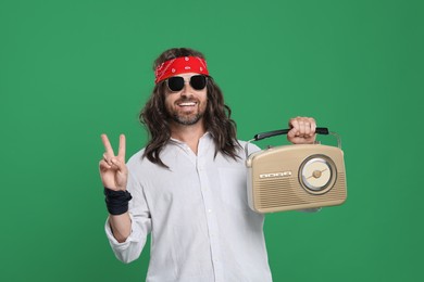 Stylish hippie man in sunglasses with retro radio receiver showing V-sign on green background