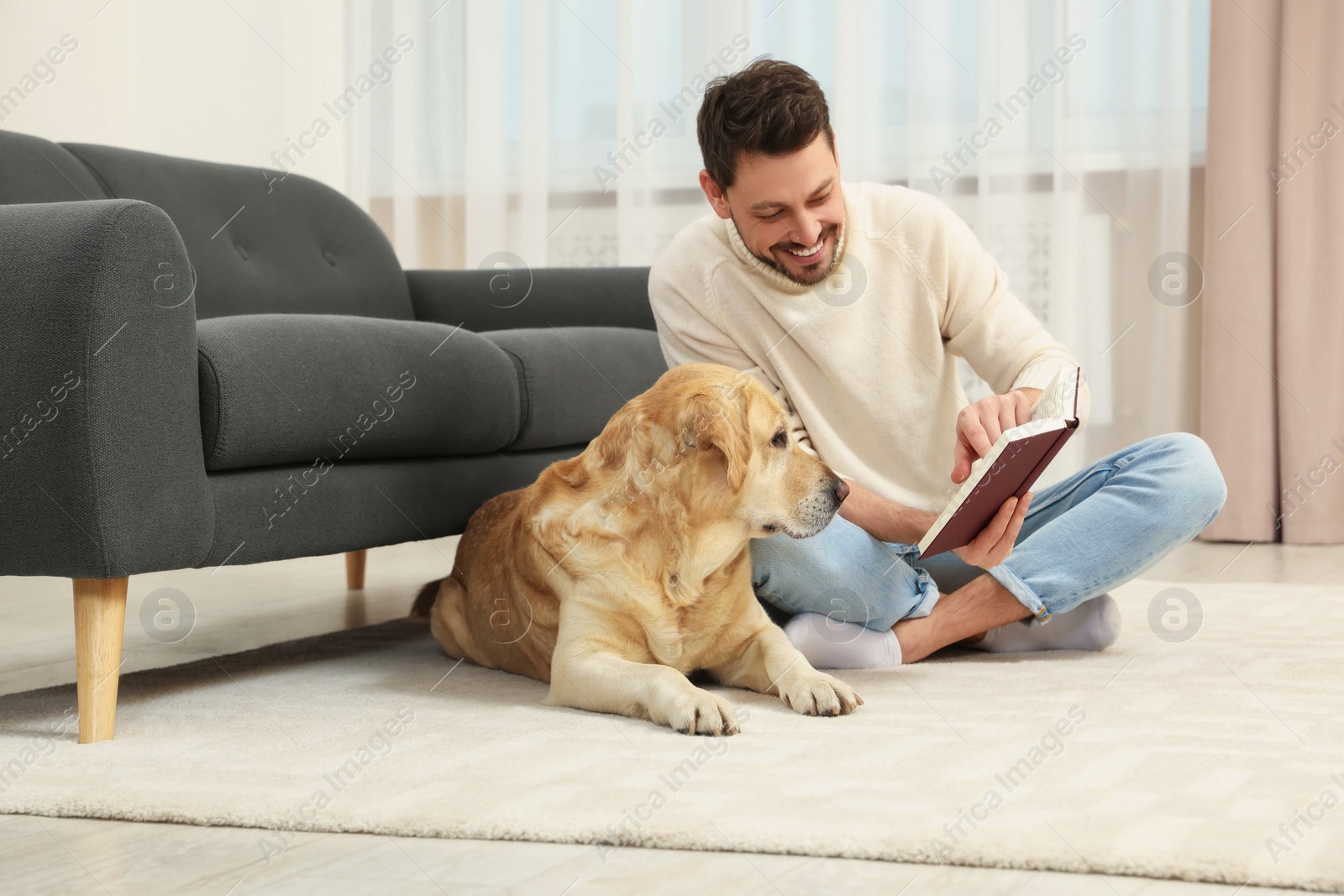 Photo of Man reading book on floor near his cute Labrador Retriever at home