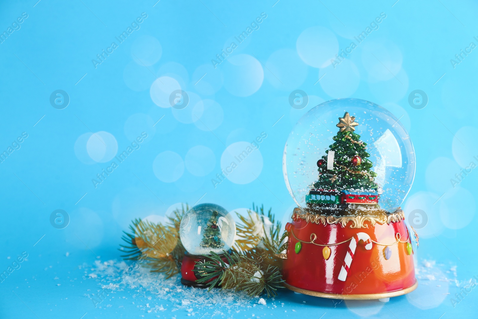 Image of Beautiful Christmas snow globes on light blue background, bokeh effect. Space for text