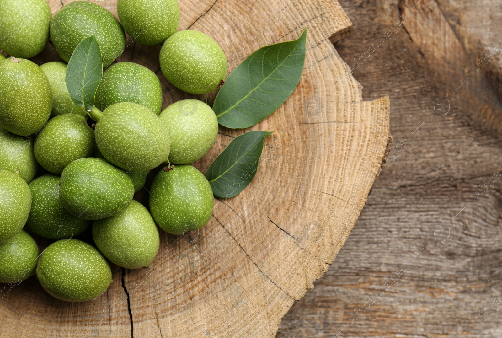 Photo of Many green walnuts and leaves on wooden stump, flat lay. Space for text