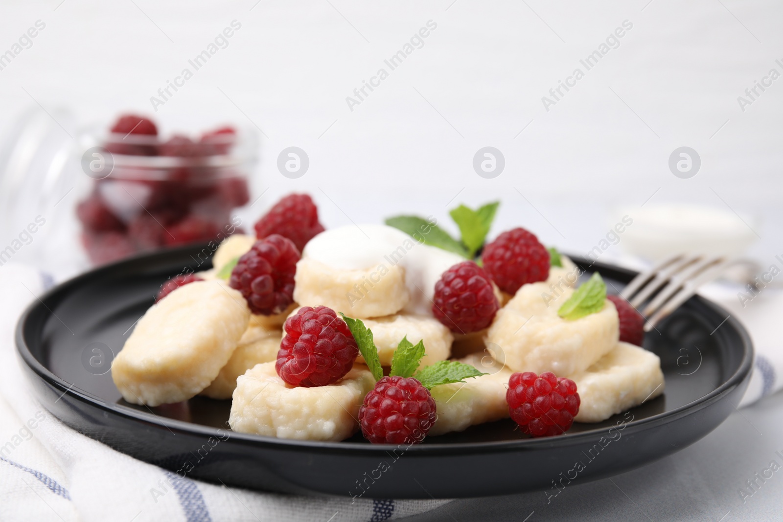 Photo of Plate of tasty lazy dumplings with raspberries, sour cream and mint leaves on white table, closeup