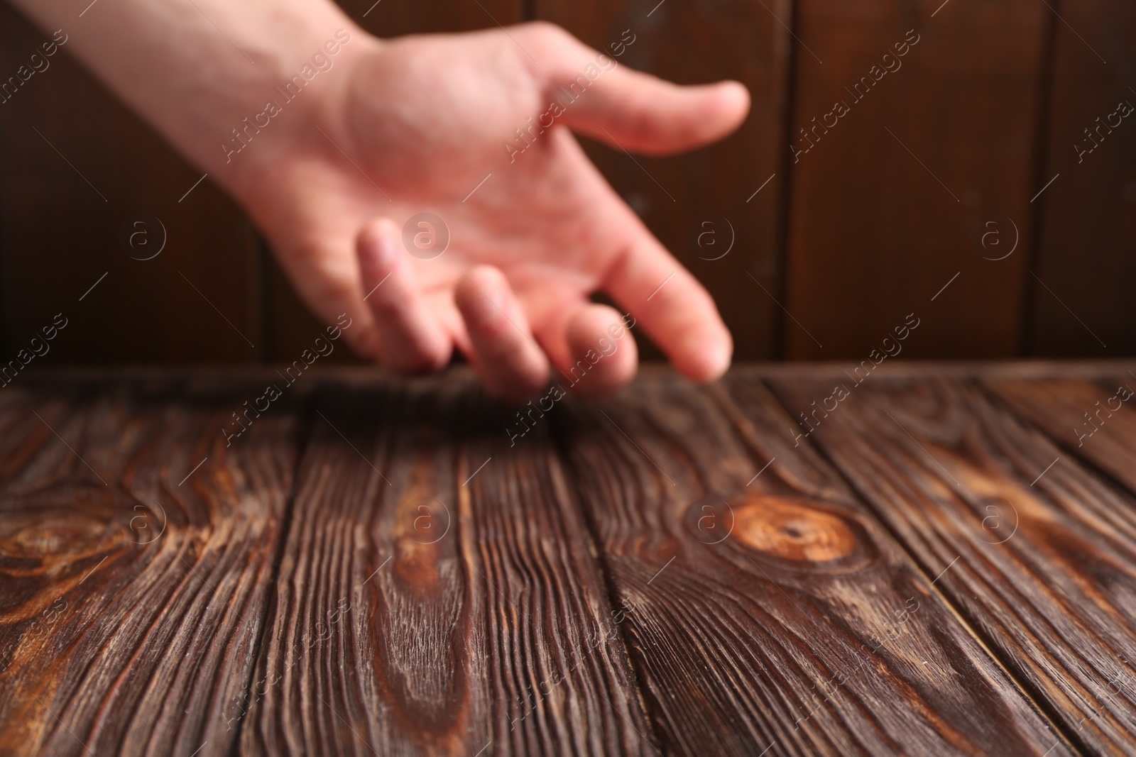 Photo of Man holding hand above wooden table, selective focus. Space for text