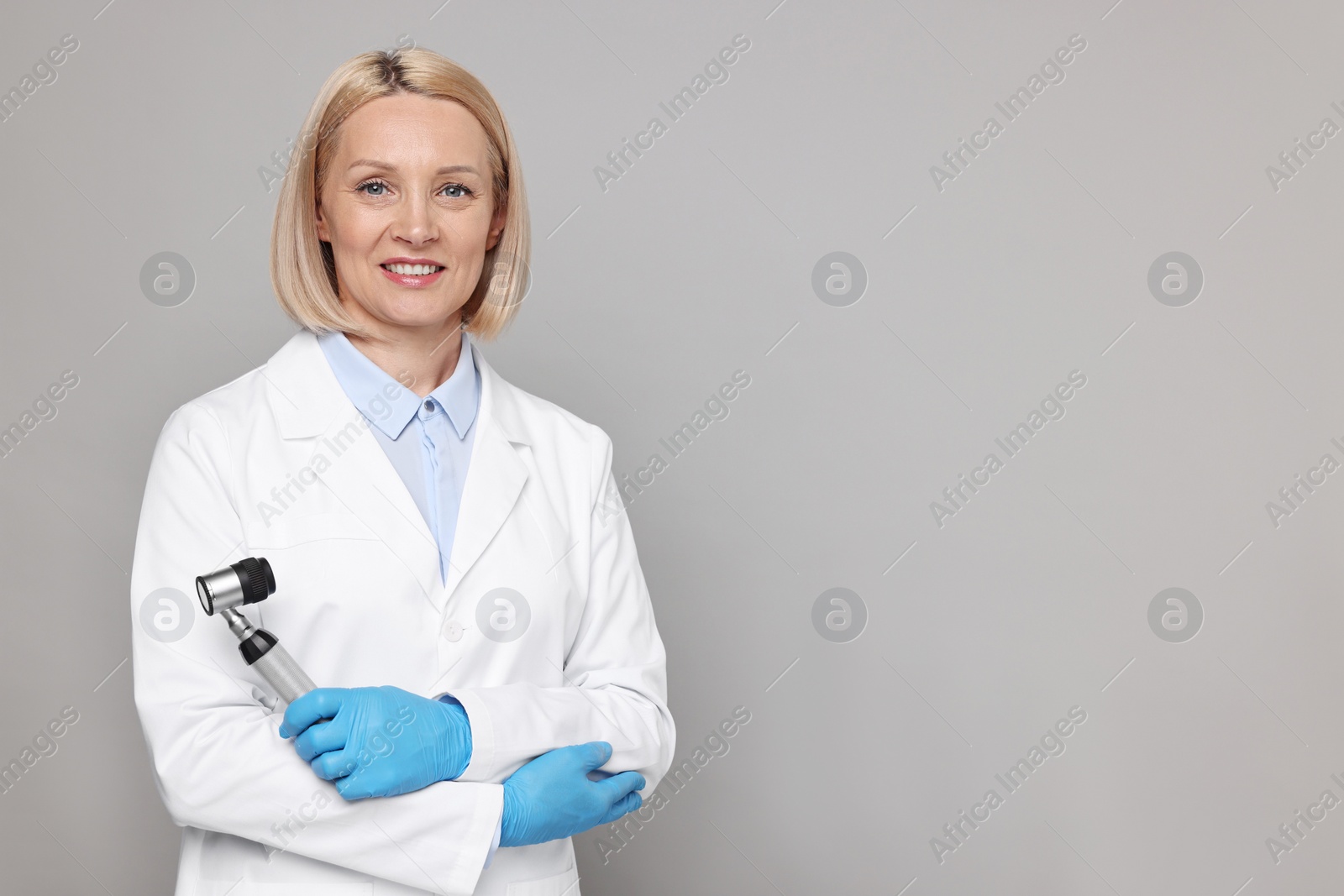 Photo of Happy dermatologist with dermatoscope on grey background, space for text